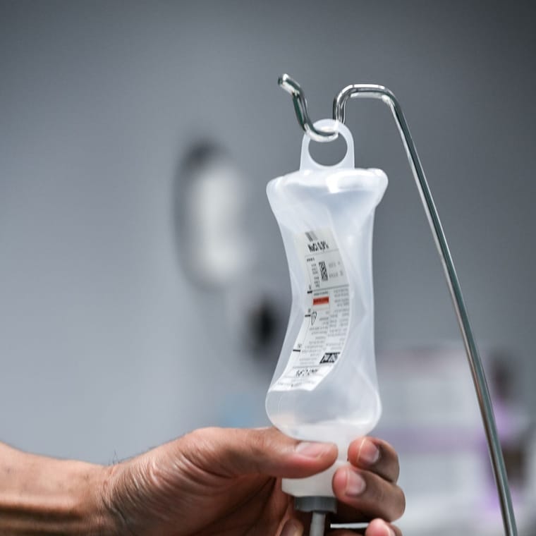 A hand adjusting an intravenous infusion bag