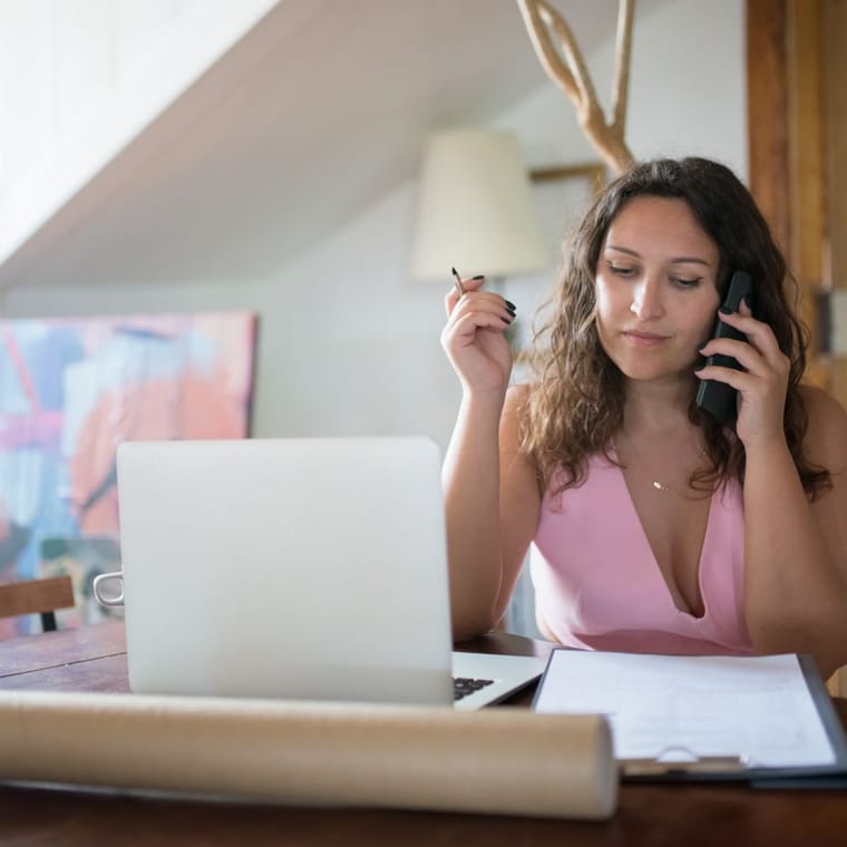A woman at a desk on the phone, with a laptop and paperwork